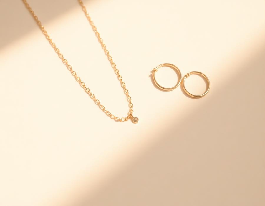 Minimal gold chain and hoop earrings on a beige surface